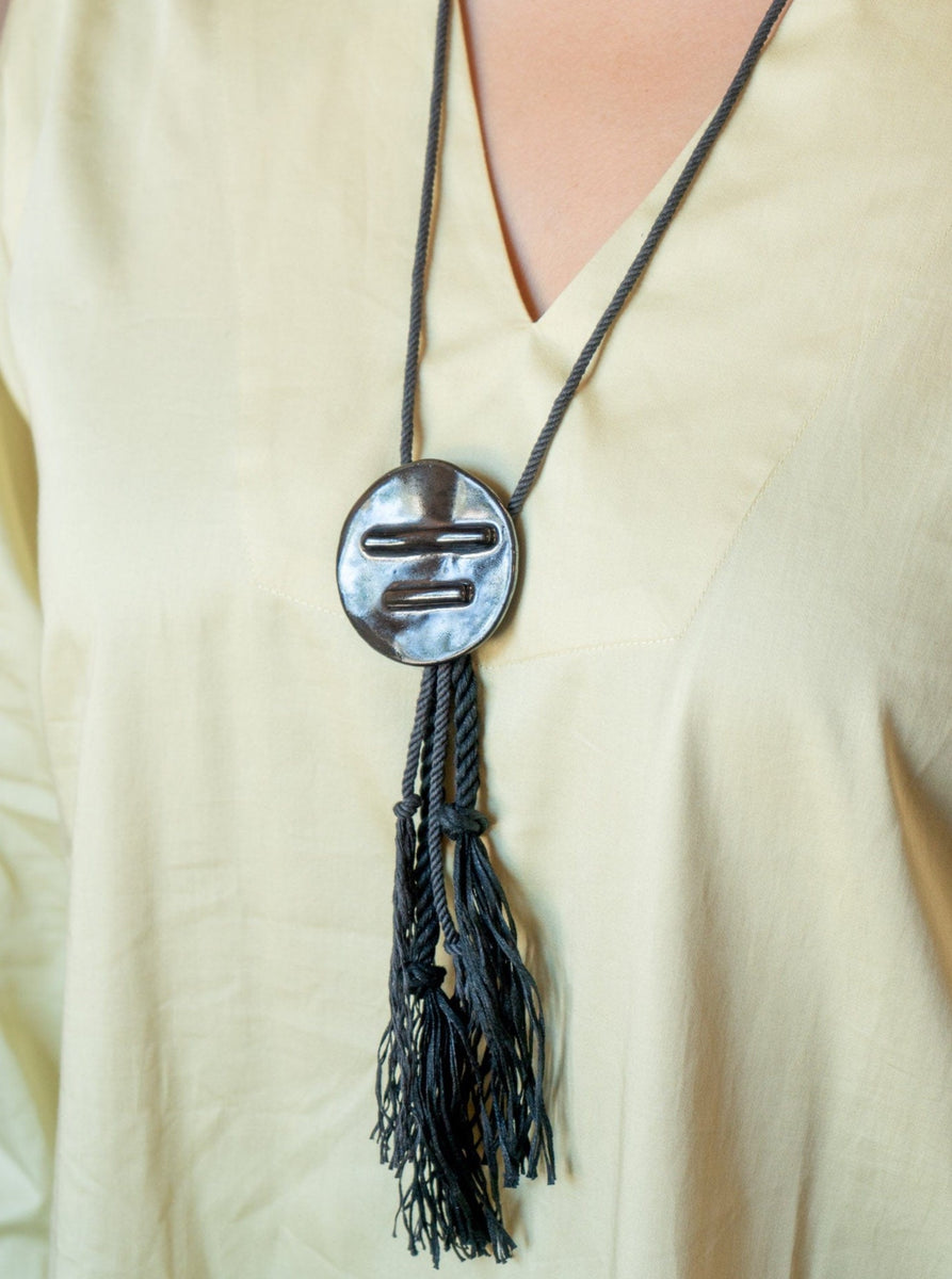 A woman wearing a yellow shirt with the Edena Necklace, a handmade black tassel necklace.