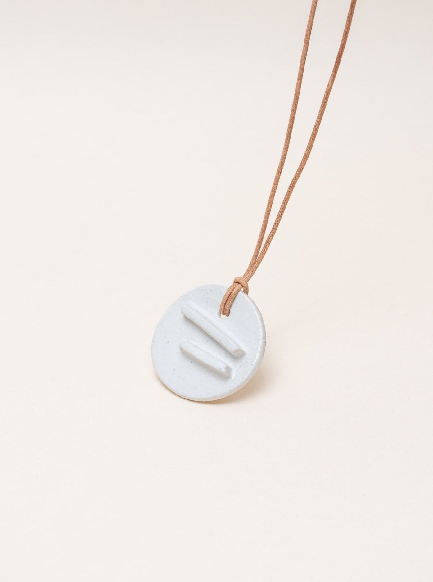 A Mini Edena Necklace with a white circle on a brown leather cord.