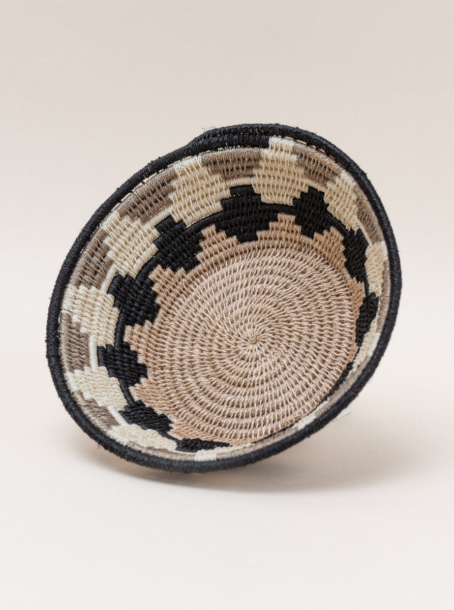 A black and white woven handmade sisal catchall basket, using Swazi weaving techniques, resting on a white surface.