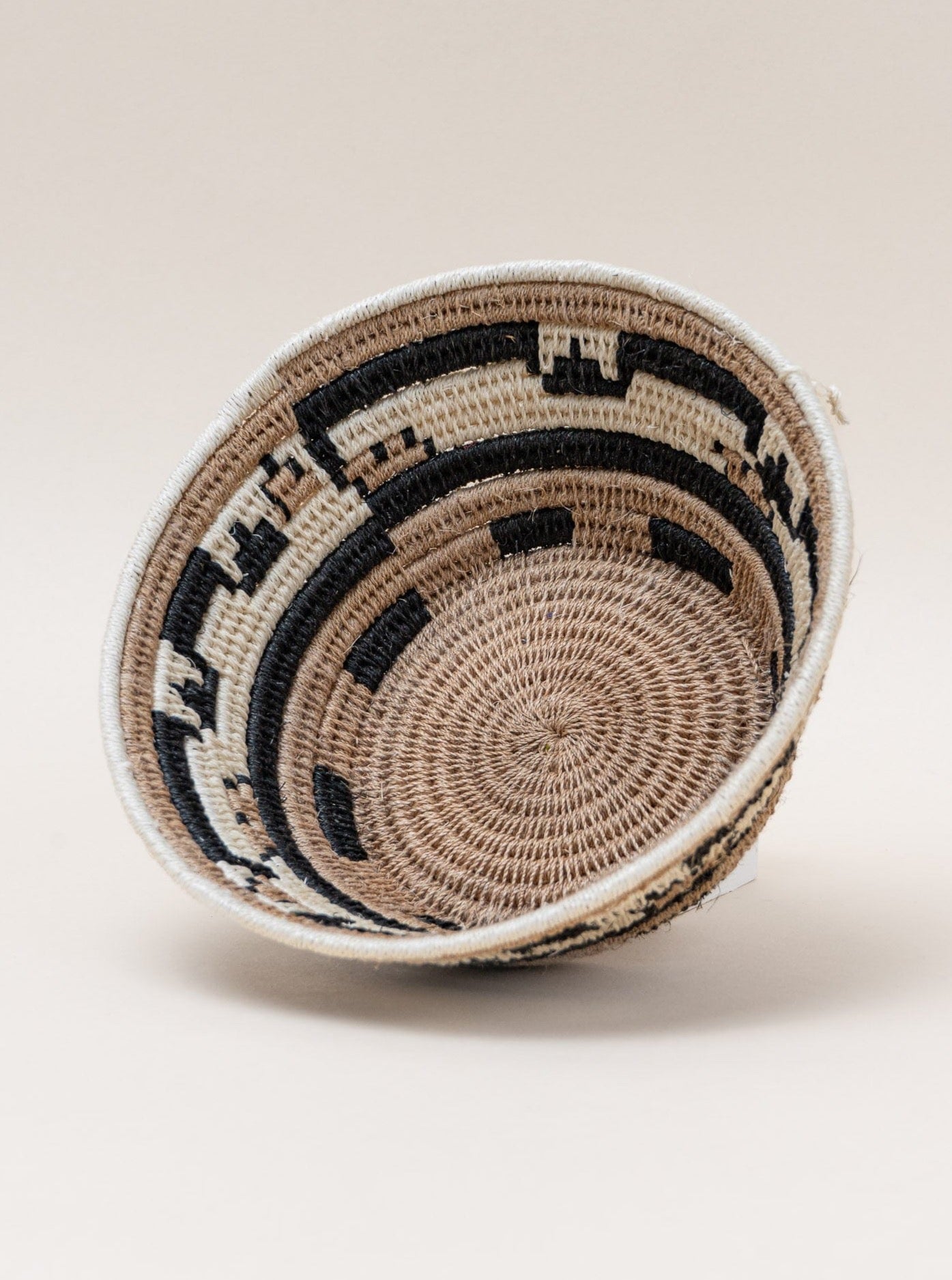 A handmade black and white woven sisal catchall basket, showcasing Swazi weaving techniques, on a white surface.
