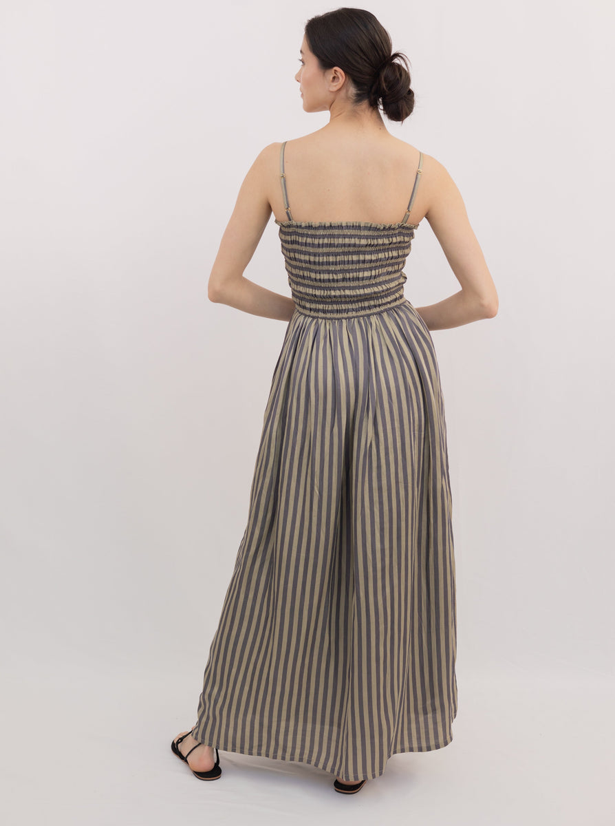 A woman standing with her back to the camera, wearing a Spaghetti Strap Maxi Dress - Urban Stripe and sandals.