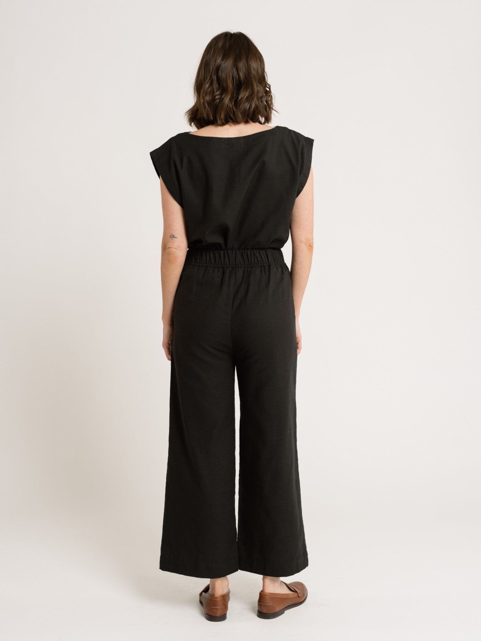 A woman in a high-waisted, wide-leg Everyday Crop Pant - Black Cotton jumpsuit.