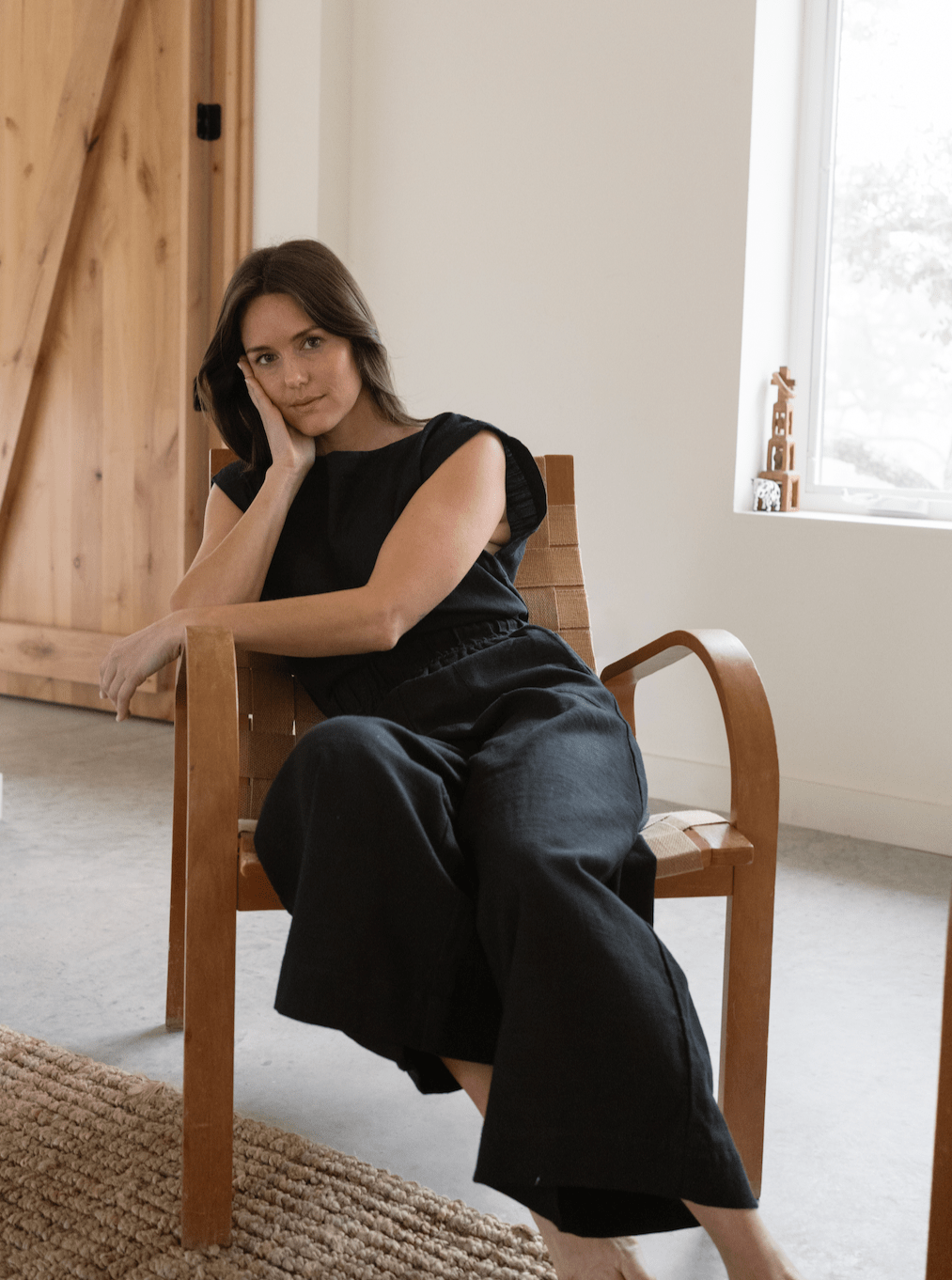 A woman sitting in a chair wearing the Everyday Crop Pant - Black Cotton.