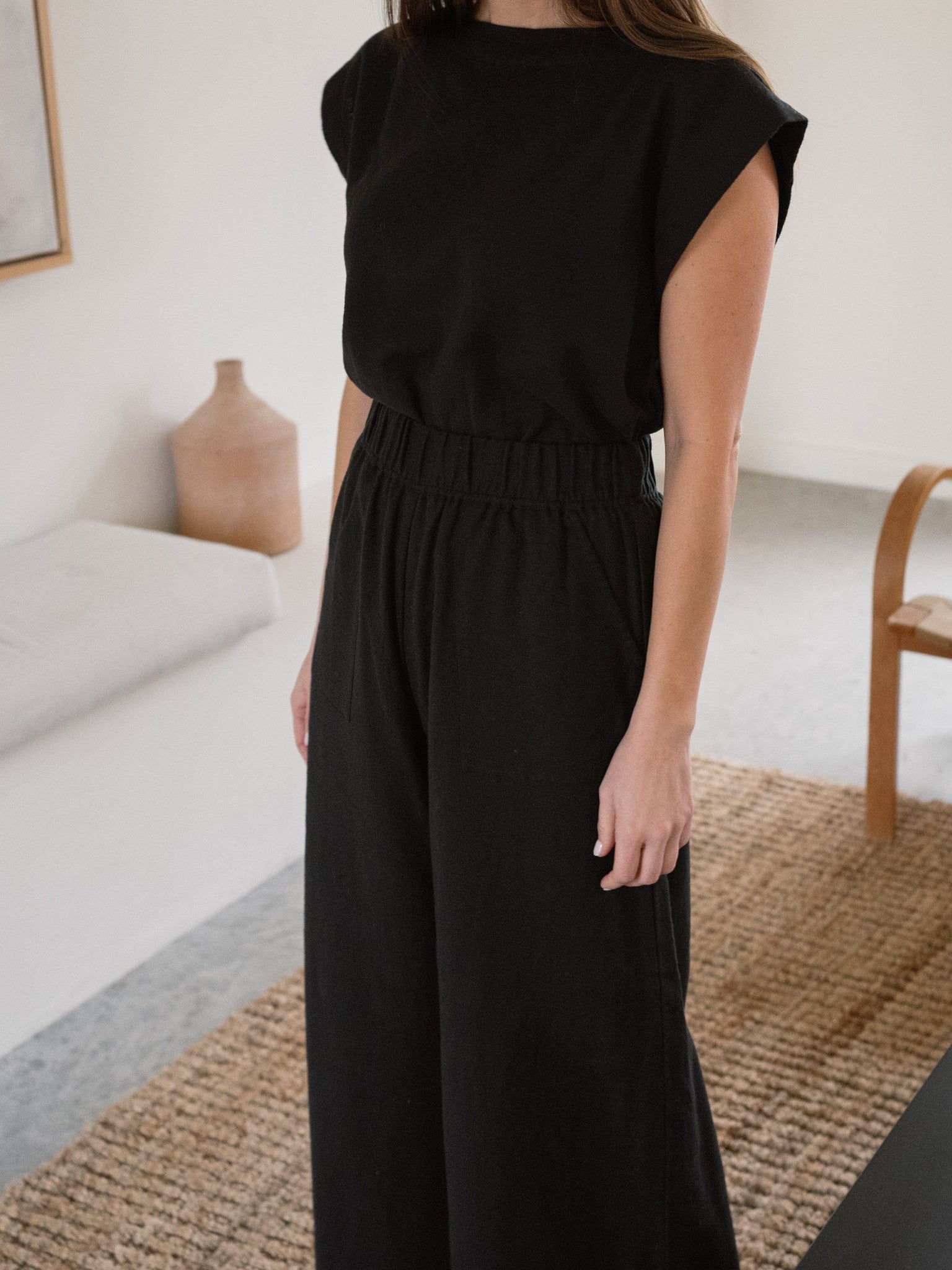 A woman standing in a living room wearing Everyday Crop Pant - Black Cotton.